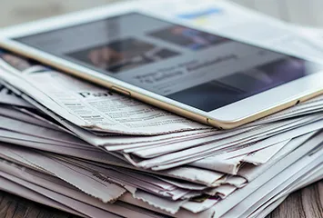 Tablet computer sitting on top of a stack of newspapers.