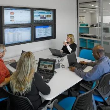 Glass-enclosed meeting rooms can be smaller, while maintaining an open feel. Here, a meeting is held at an office of Accenture, a consulting firm that has assisted on the Integrated Workplace Initiative.