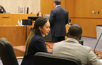 An attorney and client talk in a courtroom.